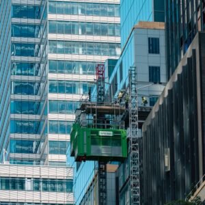 Dynamic urban construction scene in NYC featuring workers and a green hoist against glass skyscrapers.