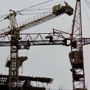 From below of metal industrial cranes located in contemporary construction site against gray sky